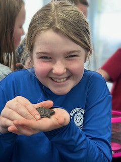 A smiling Mayflower student holding a small classroom animal